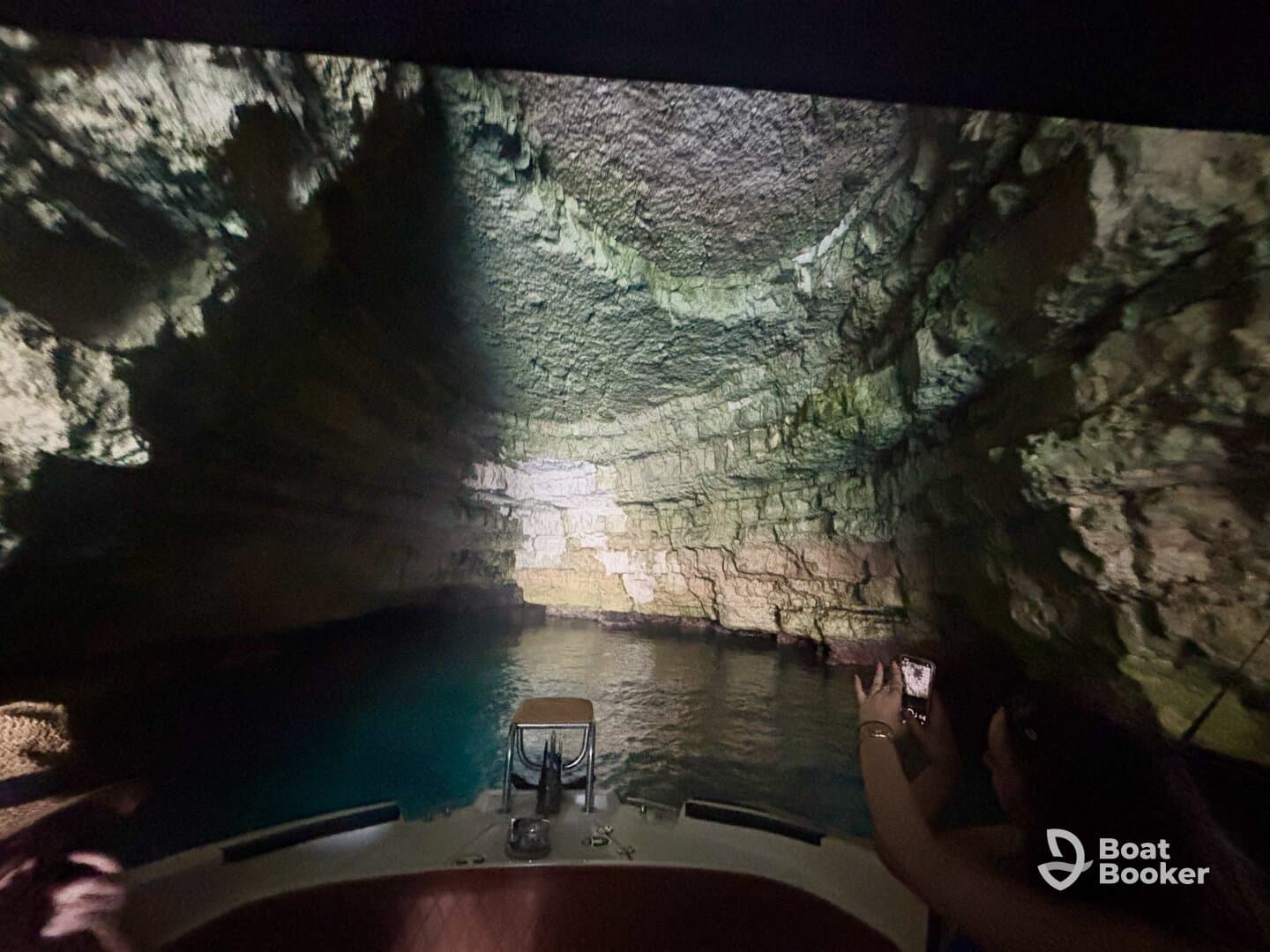 A captivating view of a cave's interior as a guest captures the moment on their phone while aboard a boat — a perfect blend of adventure and natural beauty.
