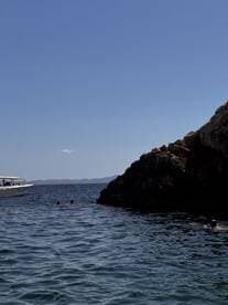 Guests enjoy a refreshing swim near a rocky coastline with a boat anchored nearby, capturing the essence of a perfect day on the water.