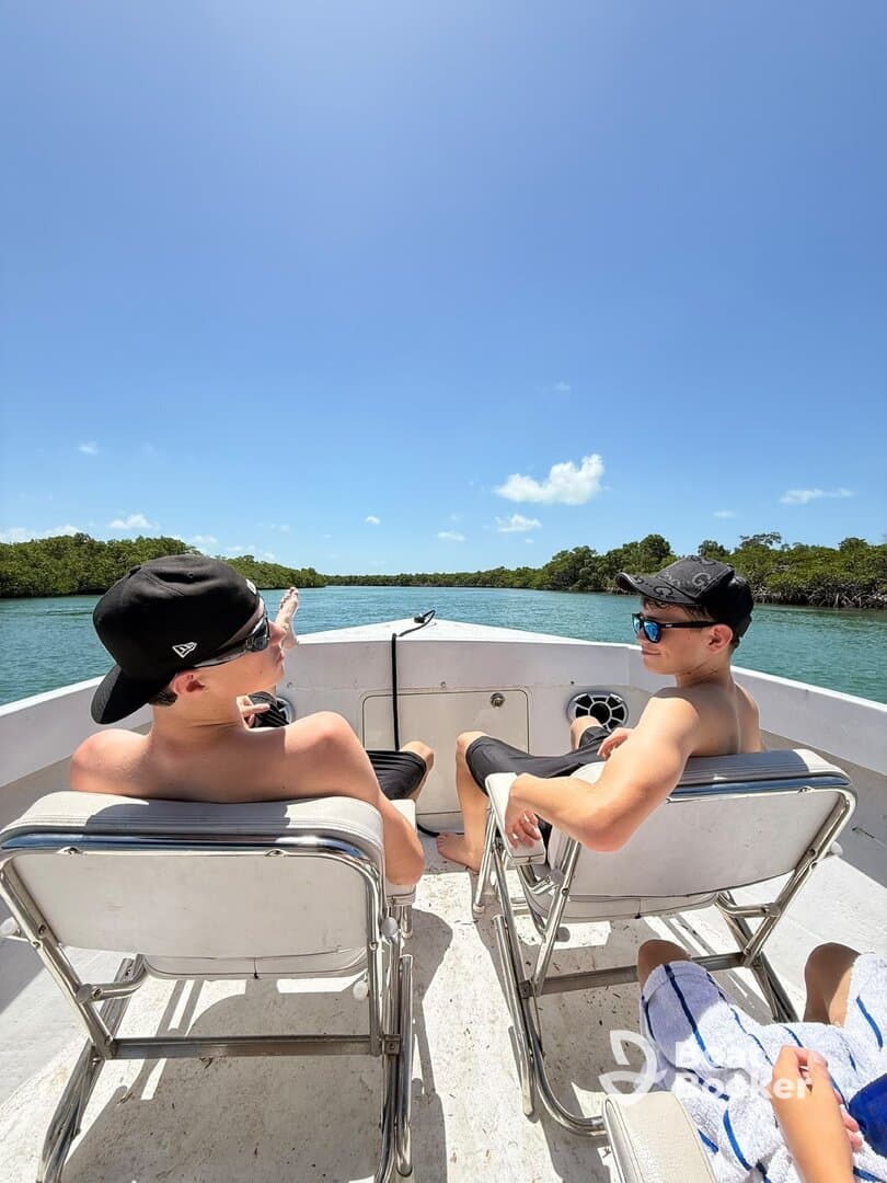 Two friends relax on a boat, enjoying the scenic views of mangroves under a clear blue sky — a perfect day for adventure and exploration.