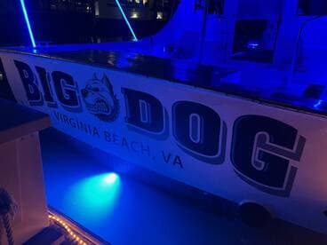The 'Big Dog' boat is illuminated in blue lights, showcasing its name and design while docked in Virginia Beach — a perfect spot for evening outings.