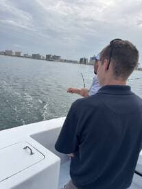 Two individuals enjoy a fishing trip on a boat, with a scenic city skyline in the background — perfect for a day of adventure on the water.