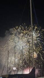 A stunning display of fireworks lights up the night sky, framed by the masts of nearby boats — a perfect backdrop for festive celebrations on the water.