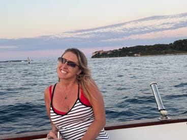 A joyful woman smiles on a boat, capturing the essence of a perfect sunset cruise — an ideal moment for relaxation and celebration on the water.