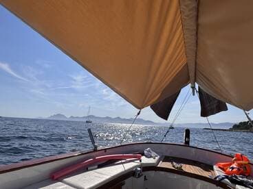 A serene view from the interior of a boat, showcasing the helm and shaded seating area, with a picturesque backdrop of distant mountains and sparkling water.