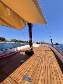 A serene view of the interior deck of a boat, showcasing the polished wooden flooring and shaded seating area, perfect for relaxing while enjoying the open water.