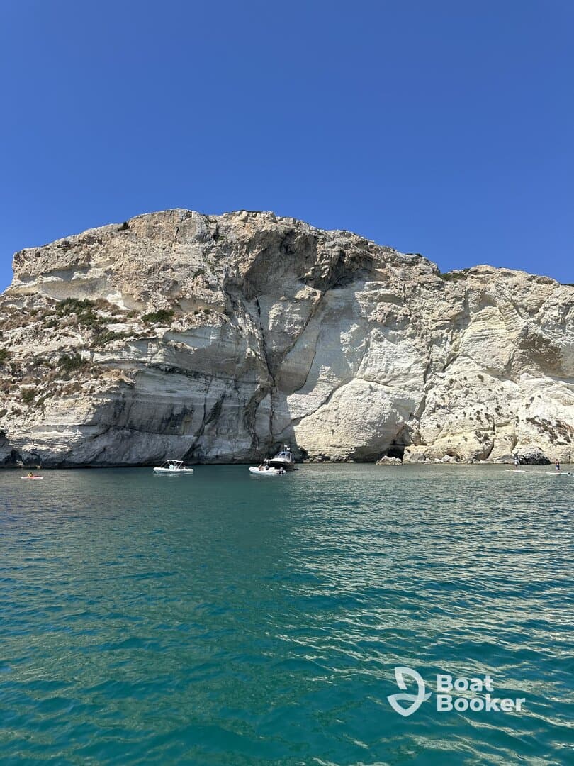 A picturesque view of a rocky coastline with boats anchored in clear waters, showcasing the beauty of a perfect day on the water.