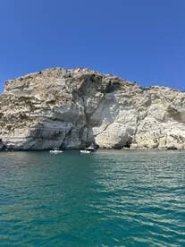 A picturesque view of a rocky coastline with boats anchored in clear waters, showcasing the beauty of a perfect day on the water.