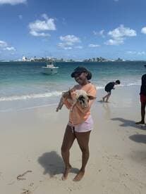 A joyful moment on the beach as a woman holds a pig, showcasing a unique wildlife interaction in a tropical setting.