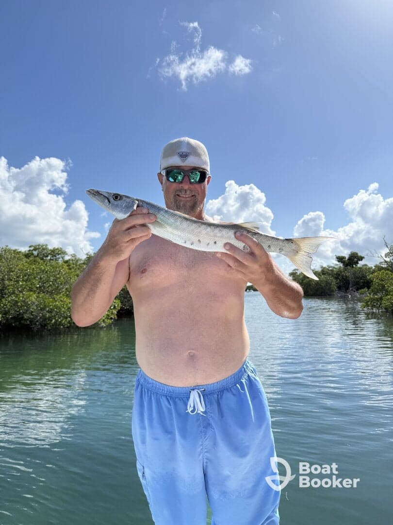 A proud angler displays his catch of the day, a barracuda, in a picturesque outdoor setting — a perfect moment for fishing enthusiasts.