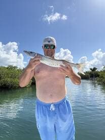 A proud angler displays his catch of the day, a barracuda, in a picturesque outdoor setting — a perfect moment for fishing enthusiasts.