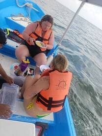 Two friends enjoy a meal on a small boat, showcasing a relaxed and fun atmosphere while out on the water.