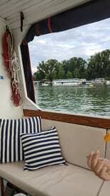 A cozy interior shot of a boat featuring striped cushions and a hand holding a snack, with a scenic view of the water and other boats in the background.