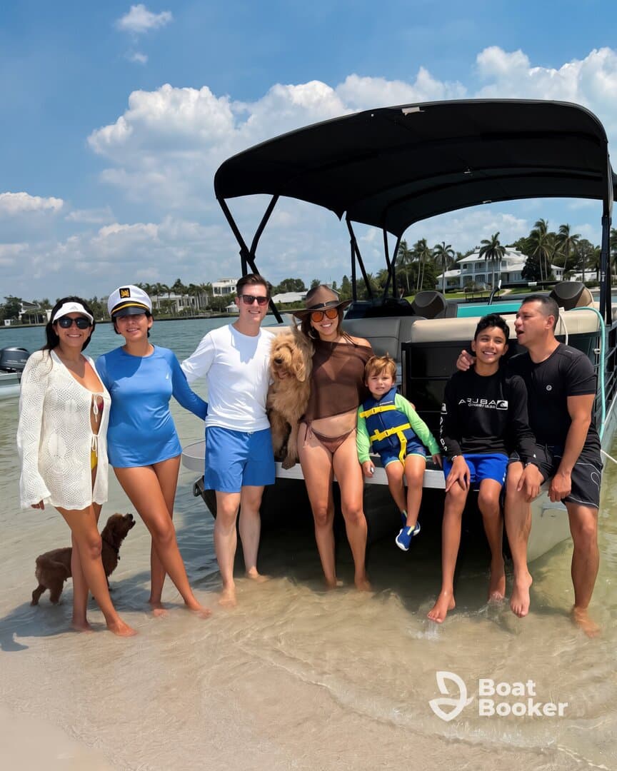 A joyful group of friends and family, including a child and a dog, enjoy a sunny day at the beach with their boat in the background, perfect for creating lasting memories on the water.