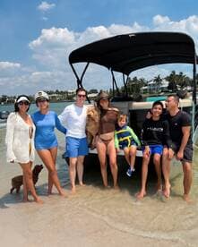 A joyful group of friends and family, including a child and a dog, enjoy a sunny day at the beach with their boat in the background, perfect for creating lasting memories on the water.