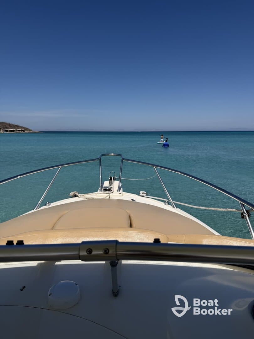 A scenic view from the bow of a boat, showcasing a paddleboarder enjoying the clear turquoise waters — perfect for water sports enthusiasts.