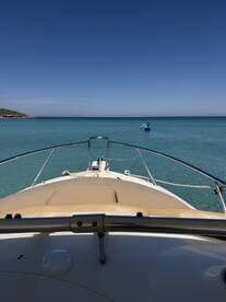 A scenic view from the bow of a boat, showcasing a paddleboarder enjoying the clear turquoise waters — perfect for water sports enthusiasts.