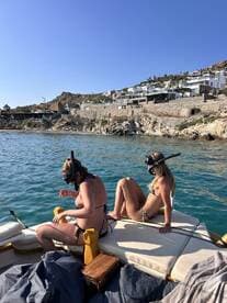 Two friends prepare for snorkeling while relaxing on the deck of a boat, surrounded by beautiful coastal scenery — a perfect day for aquatic adventures.