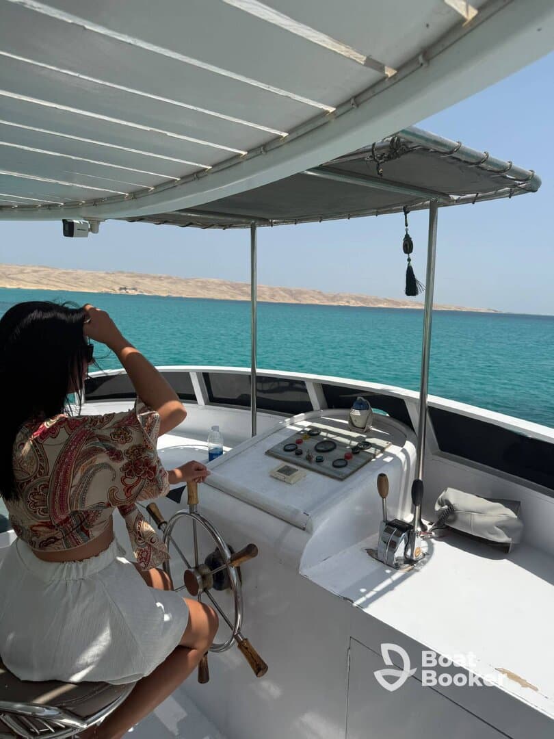 A woman navigates the helm of a boat, showcasing the interior space and steering controls against a backdrop of turquoise waters.