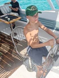 A young boy takes the helm aboard a boat, enjoying the sunny ocean views — a perfect moment of adventure on the water.