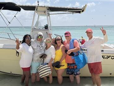 A cheerful group poses for a photo by their boat on the beach, capturing a fun day of sun and celebration on the water.
