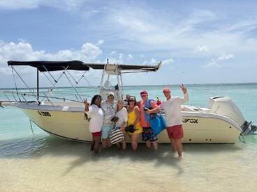 A cheerful group poses by their boat on a beautiful beach, capturing a moment of fun and celebration in the sun.