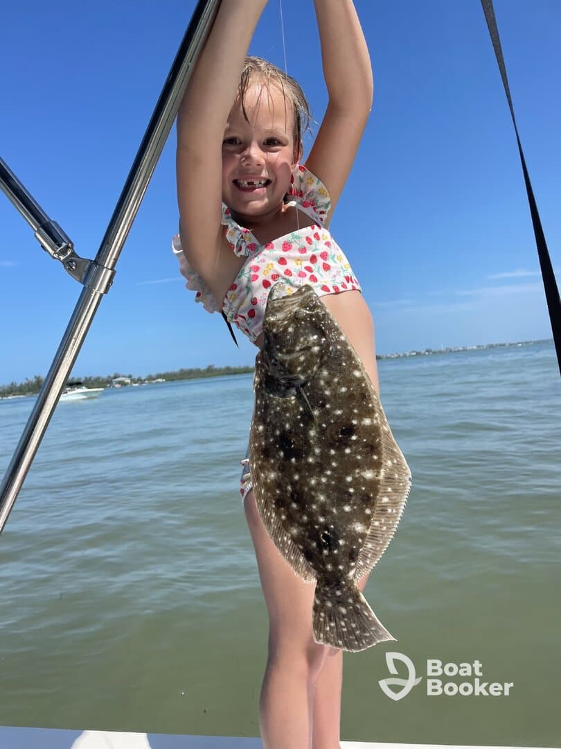 A joyful child proudly holds up a flounder caught while fishing, showcasing a fun day on the water.