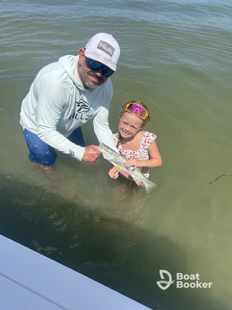 A joyful moment as a child proudly holds a fish caught while fishing with an adult in shallow waters — a perfect family fishing adventure.