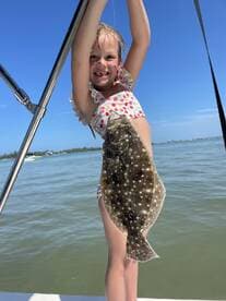 A joyful child proudly holds up a flounder caught while fishing, showcasing a fun day on the water.