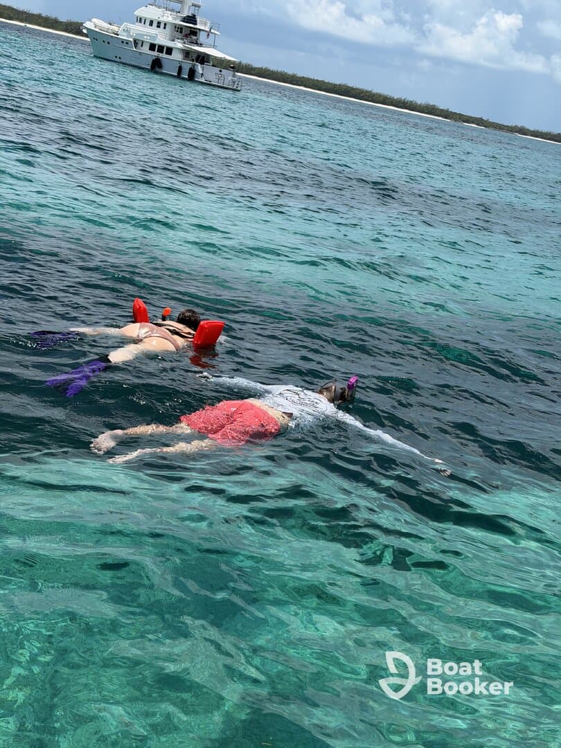 Two snorkelers enjoy exploring the vibrant underwater world in crystal-clear waters, with a boat anchored nearby, perfect for a day of aquatic adventure.