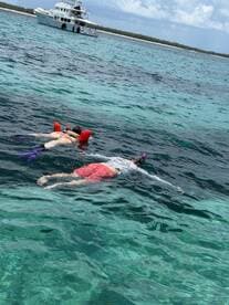 Two snorkelers enjoy exploring the vibrant underwater world in crystal-clear waters, with a boat anchored nearby, perfect for a day of aquatic adventure.