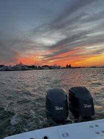 A stunning sunset view from the back of a boat, showcasing powerful Yamaha engines and a picturesque marina filled with yachts.