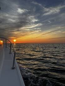 A stunning sunset view from the side of a boat, showcasing the tranquil ocean waters and vibrant sky — perfect for evening cruises.