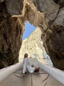 A woman relaxes on a boat while enjoying the stunning views of a rocky cave formation — a perfect moment for adventure seekers exploring coastal landscapes.