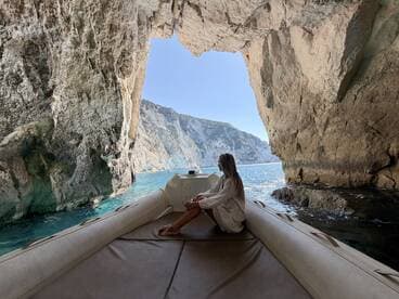 A serene moment captured inside a boat, with a woman gazing out at the stunning coastal scenery through a natural rock arch — a perfect escape into nature's beauty.