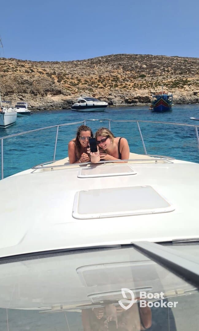 Two friends enjoy a fun moment taking a selfie on the bow of a boat, surrounded by stunning blue waters and rocky landscapes — perfect for memorable boating adventures.