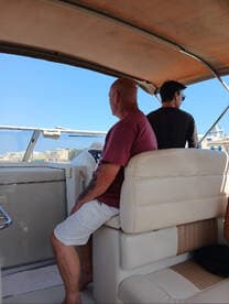 Two individuals are seated inside the helm area of a boat, enjoying the view and the experience of being on the water.