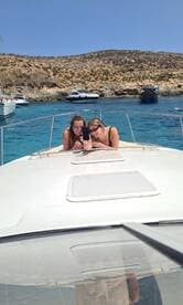 Two friends enjoy a fun moment taking a selfie on the bow of a boat, surrounded by stunning blue waters and rocky landscapes — perfect for memorable boating adventures.