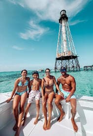 A joyful family poses on a boat with a lighthouse in the background, enjoying a sunny day at the beach — perfect for summer adventures and family outings.