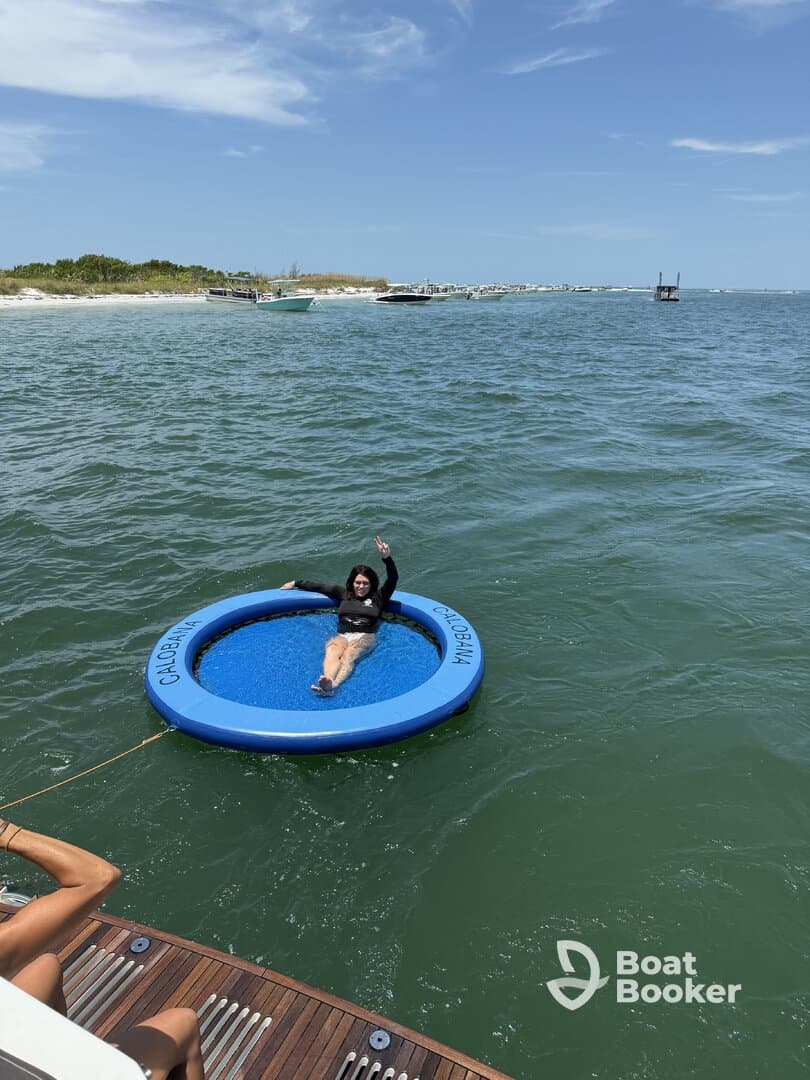 A woman enjoys a sunny day on a floating mat in the water, waving cheerfully. This scene captures the essence of fun and relaxation during a boating trip.