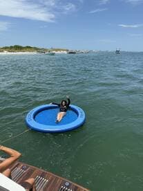 A woman enjoys a sunny day on a floating mat in the water, waving cheerfully. This scene captures the essence of fun and relaxation during a boating trip.