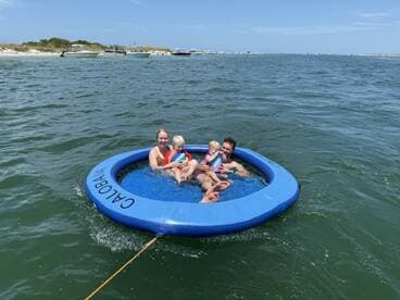 A joyful family enjoys a sunny day on a floating mat in the water, creating lasting memories of fun and laughter at the beach.
