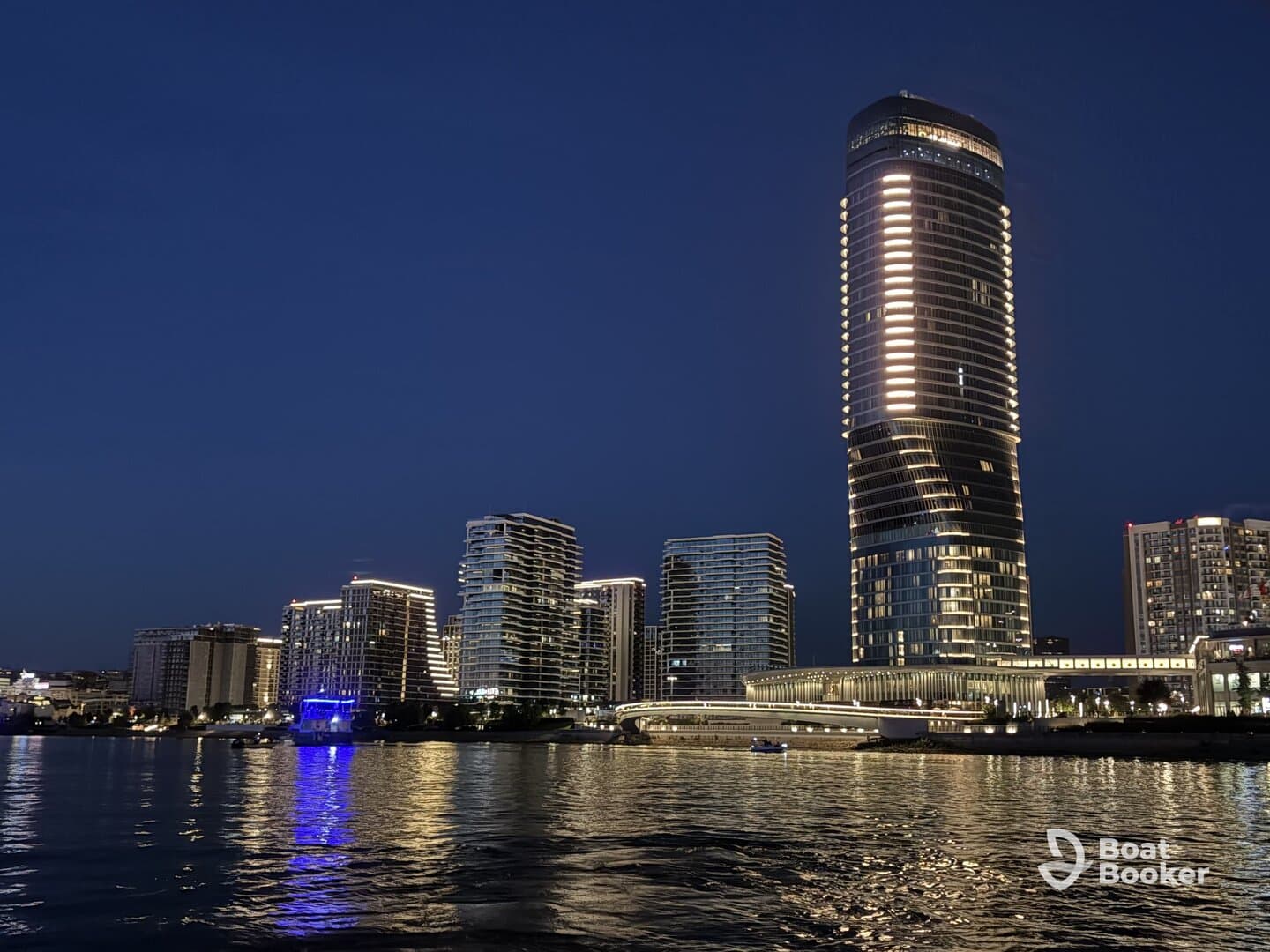 A stunning night view of illuminated skyscrapers along the waterfront, showcasing the vibrant city skyline reflected in the water.