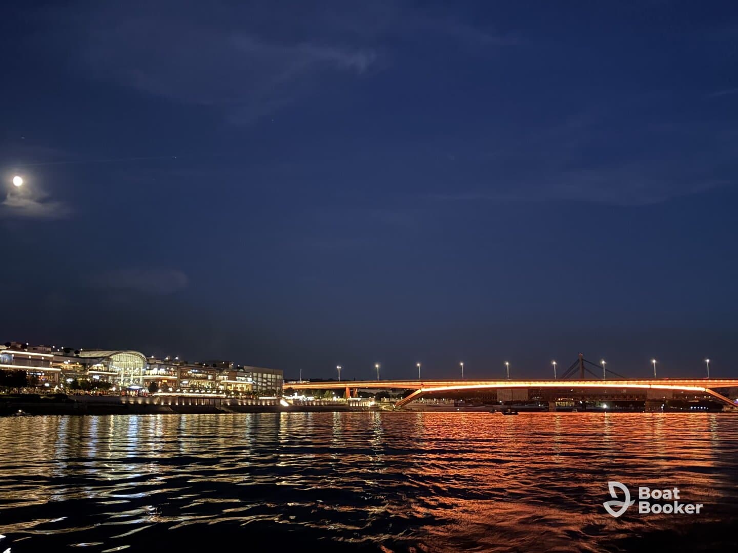 A serene night view of a cityscape illuminated by moonlight, with reflections shimmering on the water — a perfect backdrop for evening boat cruises.