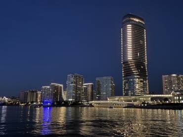 A stunning night view of illuminated skyscrapers along the waterfront, showcasing the vibrant city skyline reflected in the water.