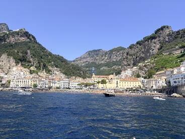 A stunning view of the Amalfi Coast showcasing colorful buildings nestled against the mountains, with boats dotting the clear blue waters — a perfect destination for scenic boat tours.