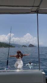 A joyful moment captured as a woman prepares to jump into the water while a man swims nearby, showcasing the fun of a day out on the boat amidst beautiful island scenery.