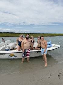A fun group poses by their boat in shallow water, enjoying a sunny day at the beach — perfect for summer adventures and memorable outings.