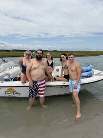 A lively group of friends enjoys a fun day at the beach, posing on their boat while wading in the water — perfect for summer adventures and memorable outings.
