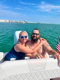 A happy couple enjoys their time on a boat, embracing and smiling against a beautiful beach backdrop — perfect for memorable summer outings.