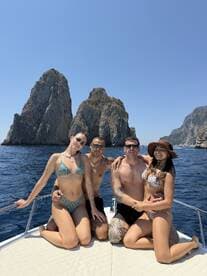 A cheerful group of friends poses on the deck of a boat, surrounded by stunning rock formations and clear blue waters — perfect for summer adventures and memorable outings.